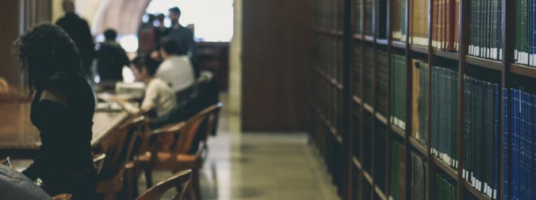 Студенты за столами в библиотеке рядом с книжными стеллажами